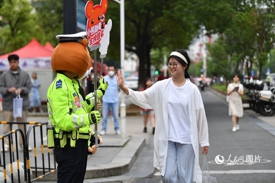6月7日上午9時(shí)，隨著鈴聲的響起，2023年江西高考正式開考，江西省的53.57萬考生以縣（區(qū)）為單位隨機(jī)安排在全省256個(gè)考點(diǎn)、18968個(gè)考場(chǎng)參加高考。圖為“小熊交警”和考生擊掌鼓勵(lì)。 人民網(wǎng)記者 時(shí)雨攝