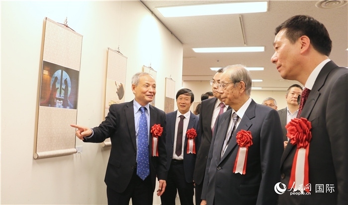 “湖州印象”攝影展主創(chuàng)、世界華人攝影協(xié)會副會長馮學(xué)敏向吳江浩大使、福田康夫前首相等嘉賓介紹展出作品。（人民網(wǎng) 許可攝）