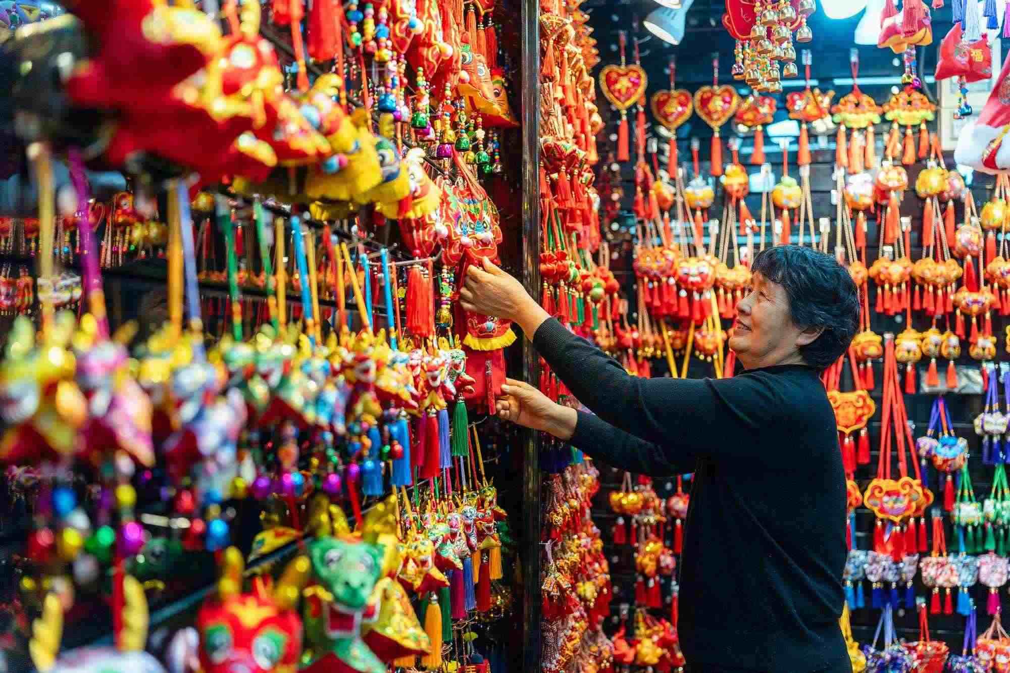 2023年12月11日，金華義烏國際商貿(mào)城，龍年喜慶用品掛滿攤位，顧客正在挑選中。