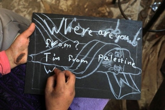 2023年12月28日，一名學(xué)生在加沙地帶南部城市拉法一所學(xué)校的臨時教室中寫下“我來自巴勒斯坦”的字樣。新華社發(fā)（里澤克·阿卜杜勒賈瓦德攝）