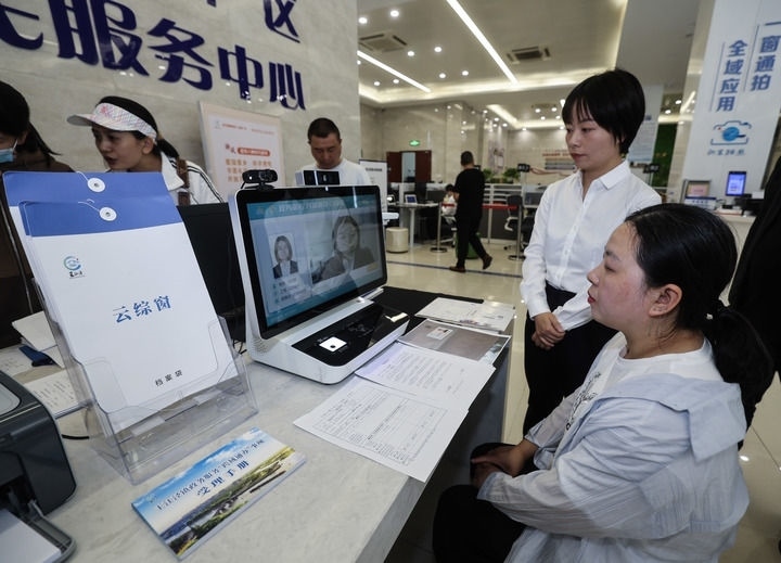 在浙江省嘉興市秀洲區(qū)王江涇鎮(zhèn)便民服務中心的“跨域通辦·云綜窗”窗口，辦理開業(yè)登記的個體工商戶（右一）通過該系統(tǒng)與江蘇省蘇州市吳江區(qū)盛澤鎮(zhèn)行政審批局工作人員視頻連線，進行身份讀取及材料線上審核（2024年5月9日攝）。新華社記者 徐昱 攝