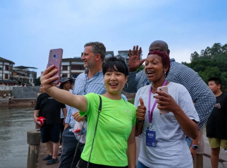 2024“一帶一路”媒體合作論壇聯(lián)合采訪調(diào)研行成員在樂(lè)山蘇稽古鎮(zhèn)與游客合影留念。本報(bào)記者 伊霄攝