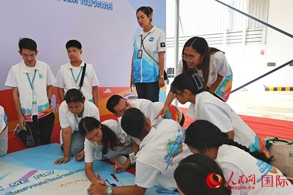 泰國學(xué)生在開營儀式展板上繪制圖案。人民網(wǎng)記者 白元琪攝